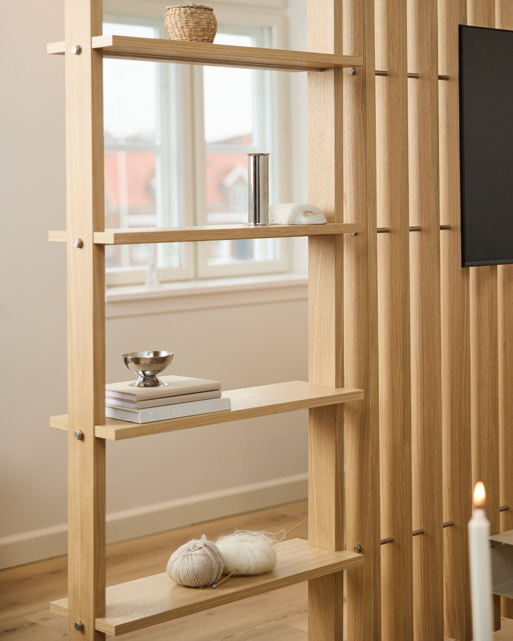 Rumsavdelare i ljus ek från WoodUpp, med vertical ribbor och hyllor med böcker och stickgarn.